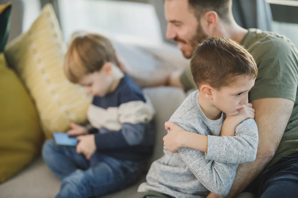 ソファで腕を組んでふてくされる子どもと、そばにいる親